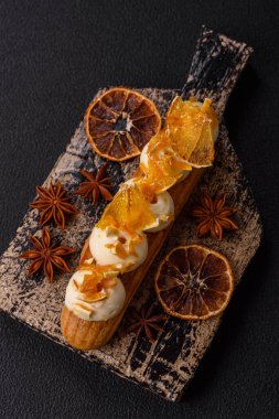 Tatlı eklerleri ya da çikolata dolgulu profiteroller ve koyu beton arka planda krema ve kurutulmuş portakallarla kaplı.