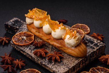 Tatlı eklerleri ya da çikolata dolgulu profiteroller ve koyu beton arka planda krema ve kurutulmuş portakallarla kaplı.