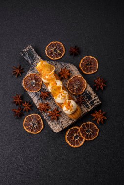 Tatlı eklerleri ya da çikolata dolgulu profiteroller ve koyu beton arka planda krema ve kurutulmuş portakallarla kaplı.