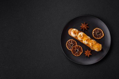 Tatlı eklerleri ya da çikolata dolgulu profiteroller ve koyu beton arka planda krema ve kurutulmuş portakallarla kaplı.