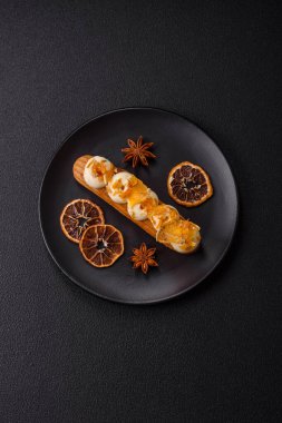 Tatlı eklerleri ya da çikolata dolgulu profiteroller ve koyu beton arka planda krema ve kurutulmuş portakallarla kaplı.