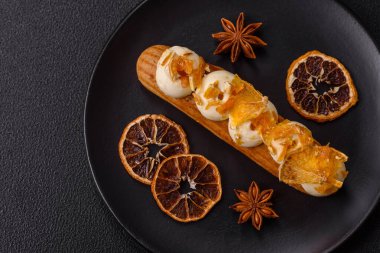 Tatlı eklerleri ya da çikolata dolgulu profiteroller ve koyu beton arka planda krema ve kurutulmuş portakallarla kaplı.