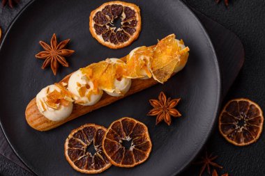 Tatlı eklerleri ya da çikolata dolgulu profiteroller ve koyu beton arka planda krema ve kurutulmuş portakallarla kaplı.