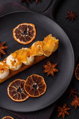 Tatlı eklerleri ya da çikolata dolgulu profiteroller ve koyu beton arka planda krema ve kurutulmuş portakallarla kaplı.