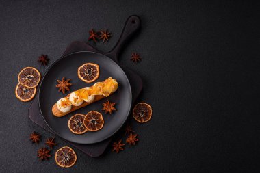 Tatlı eklerleri ya da çikolata dolgulu profiteroller ve koyu beton arka planda krema ve kurutulmuş portakallarla kaplı.