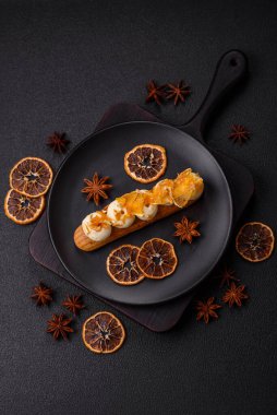 Tatlı eklerleri ya da çikolata dolgulu profiteroller ve koyu beton arka planda krema ve kurutulmuş portakallarla kaplı.