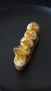 Tatlı eklerleri ya da çikolata dolgulu profiteroller ve koyu beton arka planda krema ve kurutulmuş portakallarla kaplı.