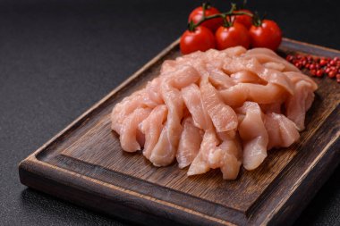 Çiğ tavuk filetosu, ahşap bir kesim tahtasının üzerinde baharat ve otlarla dilimlenmiş.