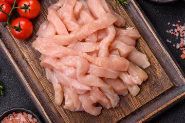 Çiğ tavuk filetosu, ahşap bir kesim tahtasının üzerinde baharat ve otlarla dilimlenmiş.