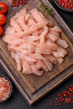 Çiğ tavuk filetosu, ahşap bir kesim tahtasının üzerinde baharat ve otlarla dilimlenmiş.