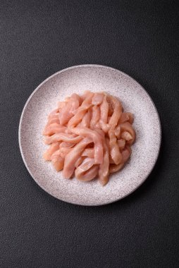 Çiğ tavuk filetosu, ahşap bir kesim tahtasının üzerinde baharat ve otlarla dilimlenmiş.