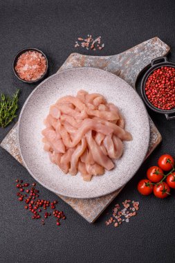 Çiğ tavuk filetosu, ahşap bir kesim tahtasının üzerinde baharat ve otlarla dilimlenmiş.