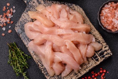 Çiğ tavuk filetosu, ahşap bir kesim tahtasının üzerinde baharat ve otlarla dilimlenmiş.