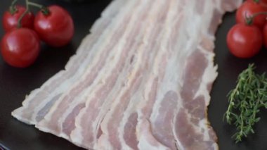 Baharat ve otlarla dilimlenmiş taze çiğ domuz pastırması ve koyu beton bir arka plan.