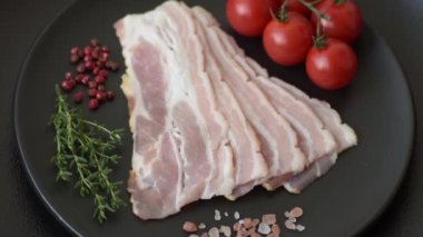 Baharat ve otlarla dilimlenmiş taze çiğ domuz pastırması ve koyu beton bir arka plan.