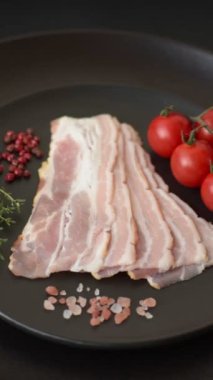 Baharat ve otlarla dilimlenmiş taze çiğ domuz pastırması ve koyu beton bir arka plan.