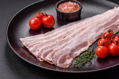 Baharat ve otlarla dilimlenmiş taze çiğ domuz pastırması ve koyu beton bir arka plan.