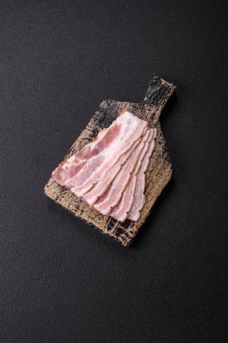 Baharat ve otlarla dilimlenmiş taze çiğ domuz pastırması ve koyu beton bir arka plan.