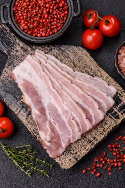 Baharat ve otlarla dilimlenmiş taze çiğ domuz pastırması ve koyu beton bir arka plan.