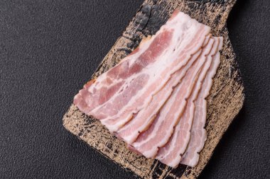 Baharat ve otlarla dilimlenmiş taze çiğ domuz pastırması ve koyu beton bir arka plan.