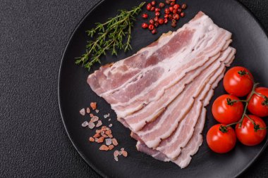 Baharat ve otlarla dilimlenmiş taze çiğ domuz pastırması ve koyu beton bir arka plan.