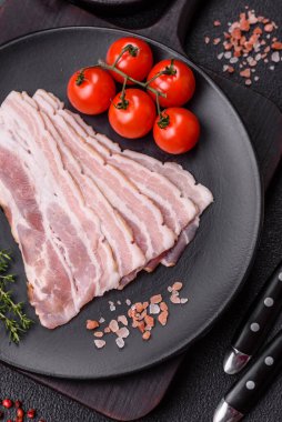 Baharat ve otlarla dilimlenmiş taze çiğ domuz pastırması ve koyu beton bir arka plan.
