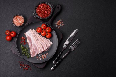 Baharat ve otlarla dilimlenmiş taze çiğ domuz pastırması ve koyu beton bir arka plan.