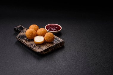 Ekmekli peynirli patates kızartması topları ya da koyu beton arka planda tatlı çilek soslu camembert peyniri.
