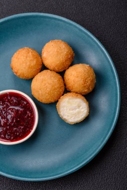 Ekmekli peynirli patates kızartması topları ya da koyu beton arka planda tatlı çilek soslu camembert peyniri.