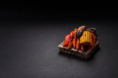 Izgara sebzeler, biberler, domatesler, kabaklar, soğanlar, havuçlar, mısır, tuzlu mantarlar, baharatlar ve otlar koyu beton arka planda.