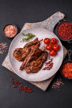 Izgarada pişmiş biftek, tuz, baharat ve otlarla birlikte koyu beton bir arka planda.