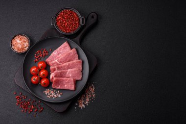 Koyu beton zeminde tuz, baharat ve otlarla dilimlenmiş sulu sığır eti.