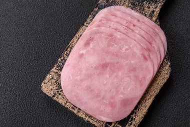 Jambon, tuzlu konserve jambon, baharat ve otlar koyu beton arka planda dilimler halinde kesilmiş.