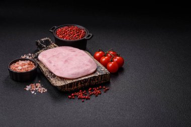 Jambon, tuzlu konserve jambon, baharat ve otlar koyu beton arka planda dilimler halinde kesilmiş.