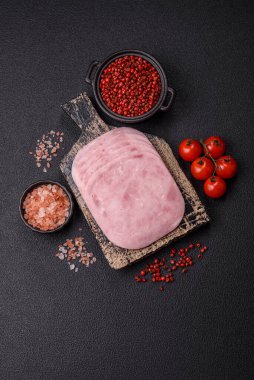 Jambon, tuzlu konserve jambon, baharat ve otlar koyu beton arka planda dilimler halinde kesilmiş.