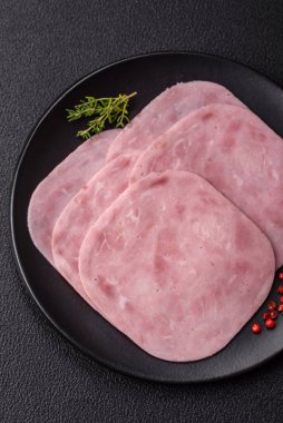 Jambon, tuzlu konserve jambon, baharat ve otlar koyu beton arka planda dilimler halinde kesilmiş.