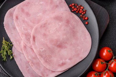 Jambon, tuzlu konserve jambon, baharat ve otlar koyu beton arka planda dilimler halinde kesilmiş.