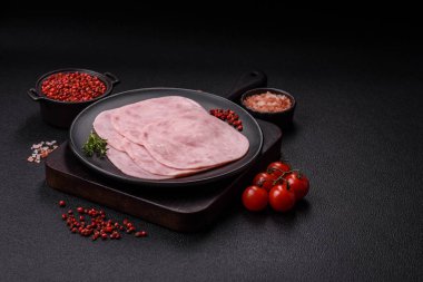 Jambon, tuzlu konserve jambon, baharat ve otlar koyu beton arka planda dilimler halinde kesilmiş.