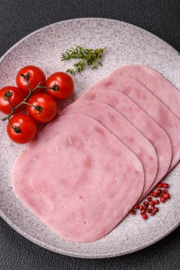 Jambon, tuzlu konserve jambon, baharat ve otlar koyu beton arka planda dilimler halinde kesilmiş.