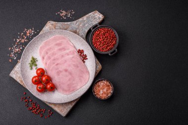 Jambon, tuzlu konserve jambon, baharat ve otlar koyu beton arka planda dilimler halinde kesilmiş.