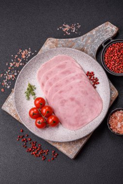Jambon, tuzlu konserve jambon, baharat ve otlar koyu beton arka planda dilimler halinde kesilmiş.
