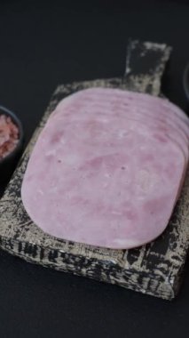 Jambon, tuzlu konserve jambon, baharat ve otlar koyu beton arka planda dilimler halinde kesilmiş.