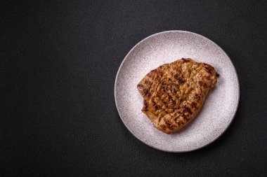 Koyu beton bir arka planda ızgara biftek veya tuzlu, baharatlı ve otlu domuz eti.