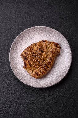 Koyu beton bir arka planda ızgara biftek veya tuzlu, baharatlı ve otlu domuz eti.