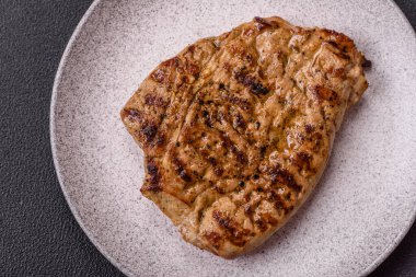 Koyu beton bir arka planda ızgara biftek veya tuzlu, baharatlı ve otlu domuz eti.