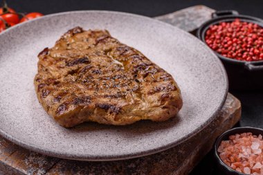 Koyu beton bir arka planda ızgara biftek veya tuzlu, baharatlı ve otlu domuz eti.