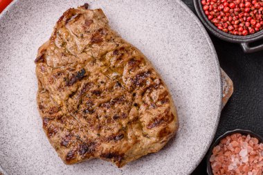 Koyu beton bir arka planda ızgara biftek veya tuzlu, baharatlı ve otlu domuz eti.