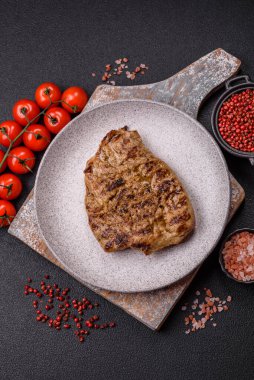 Koyu beton bir arka planda ızgara biftek veya tuzlu, baharatlı ve otlu domuz eti.