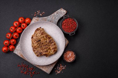 Koyu beton bir arka planda ızgara biftek veya tuzlu, baharatlı ve otlu domuz eti.