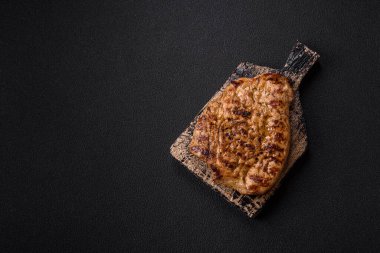 Koyu beton bir arka planda ızgara biftek veya tuzlu, baharatlı ve otlu domuz eti.